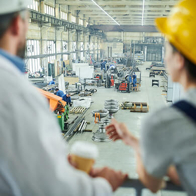 Two workers look down at a large production hall